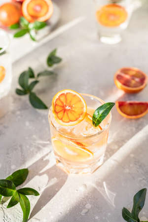 Cold refreshing drink with tonic, blood Sicilian oranges and ice, grey concrete background. Cocktail with tonic and oranges. Direct sunlight and hard shadows.の写真素材