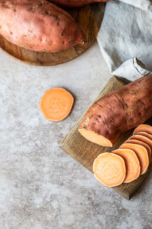 Whole and slices raw sweet potatoes on wooden board, organic yam. The farm food.の写真素材