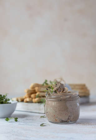 Homemade liver pate, spread or mousse in glass jar with grissini and microgreens, concrete...