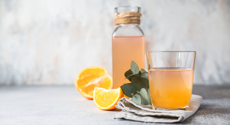 Cold and refreshing fresh orange juice in glass and bottle with fresh orange, grey background. Copy...