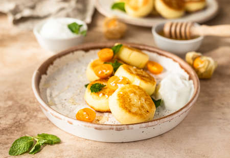 Curd or ricotta fritters with physalis, honey, yogurt and mint on ceramic plate. Cottage cheese pancakes or syrniki. Healthy and tasty breakfast.の写真素材