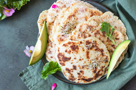 Homemade chapati or roti flatbread with green salad mix, avocado and sprouts on concrete background....