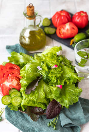 Plate with fresh green salad, gray tiled background. Mix of salad leaves with cucumber, tomatoes and...