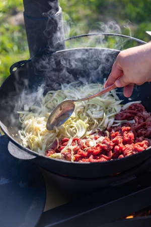 The process of cooking lagman in a cauldron on an open fire. Cooking a traditional dish of Middle East cuisine with homemade noodles, beef and vegetables. outdoor cooking.の写真素材