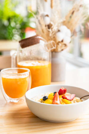 Healthy breakfast in cafe with oatmeal porridge with berries, banana and mango in bowl and spicy sea...