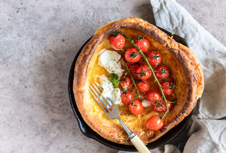 Savory Dutch baby pancake with roasted cherry tomatoes, mozzarella cheese and green salad leaves in...