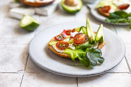 Bagels sandwich topped with cream cheese, farm cottage cheese, avocado, tomatoes, cucumbers and...