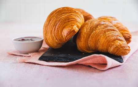 Fresh crispy croissants with red berry jam on black slate board, pink background. French croissants. Homemade bakery for tasty breakfast.の写真素材