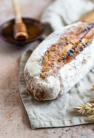Loaf of artisan sourdough bread with lavender and honey on linen napkin with wheat ears, concrete...