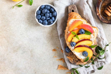 Vegetarian croissant sandwiches with nectarine, soft or cream cheese, blueberries and honey, concrete background. Healthy breakfast or lunch.の写真素材
