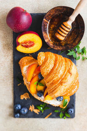 Vegetarian croissant sandwiches with nectarine, soft or cream cheese, blueberries and honey, concrete background. Healthy breakfast or lunch.の写真素材
