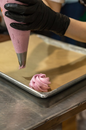 Process of marshmallow making. Chef squeezing pink meringue dessert from pastry bag on baking sheet....