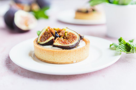 Tartlets pastry with white cream, topped with figs and pistachio, pink background. Cooking concept. Healthy dessert.の写真素材