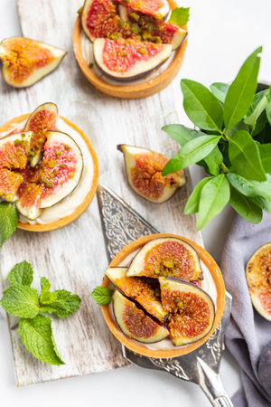 Tartlets with delicate cream cheese and fresh figs decorated with mint and pistachio, gray background. autumn dessert. National Dessert Day, October 14.の写真素材