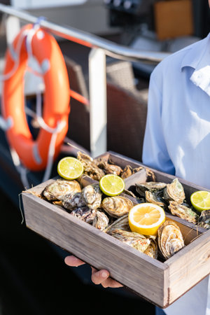 A variety of fresh oysters with lime and lemon in a wooden box. fresh seafood. outdoor cafe terrace. Blurred background with a view of the yacht club.の写真素材