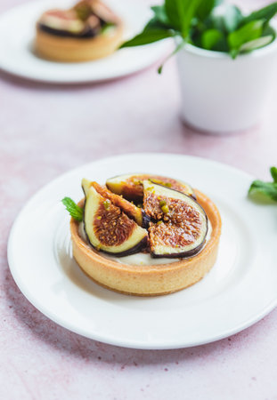 Tartlets pastry with white cream, topped with figs and pistachio on pink background. Cooking...