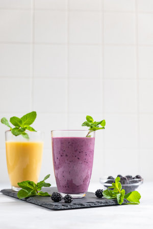 Purple and yellow fruit smoothies or milkshakes with blackberry and mint on gray concrete background. The concept of healthy, detox and dietary nutrition.の写真素材