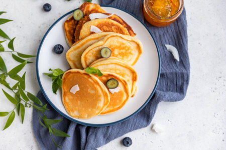 Traditional fluffy pancakes with orange jam, blueberries, coconut chips and mint for healthy...