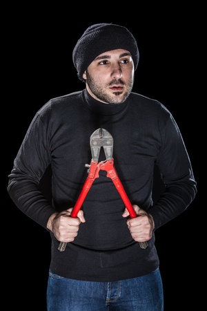 a burglar wearing black clothes holding huge wire cutters over black backgroundの写真素材