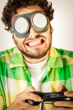 a guy wearing casual clothes and on old pair of goggles over a white bachground and using a gamepad controllerの写真素材