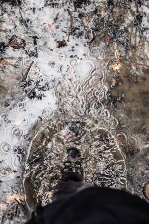 subjective view of a man stepping in a puddle with a hiking bootの写真素材