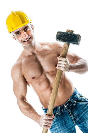 a very muscular and handsome manual worker with a sludgehammer and a yellow helmet isolated over whiteの写真素材