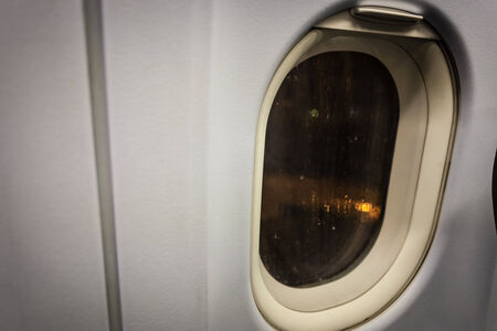 the window of a commercial airplane in a dark and rainy nightの写真素材
