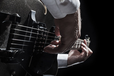 a young jazzer with a black acoustig guitar over black background