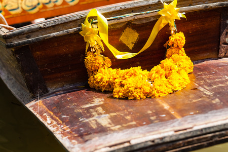 a traditional thai marigold garland on the front of a wooden boatの写真素材