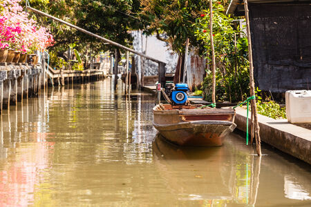 a small thai wooden motorboat in a dirty water canalの写真素材