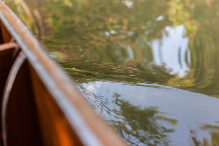 water ripple on the side of a small long tail wooden boat sailing in a countryside canal in thailandの写真素材