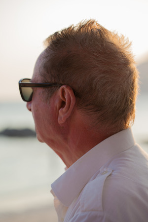 portrait shot of an old man on the beach looking at the sunsetの写真素材
