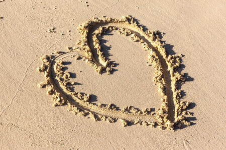 a heart shape drawn on the sand in a sunny beachの写真素材