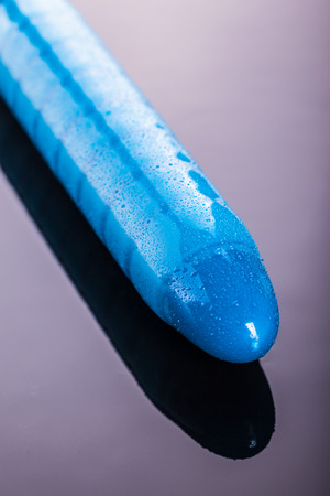 a wet blue ridged rubber dildo vibrator over a dark reflective surfaceの写真素材