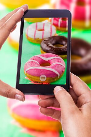 a woman using a smart phone to take a photo of some colorful donutsの写真素材