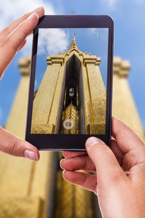 a woman using a smart phone to take a photo of an ancient temple in thailandの写真素材
