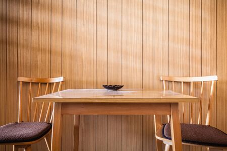 a wooden table against a wooden wall with two wooden chairs in the morningの写真素材