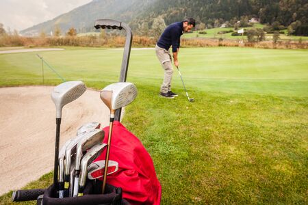 a golf player playing on a beautiful golf course and a golf bag full of golf clubsの写真素材