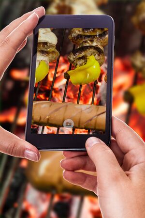 a woman using a smart phone to take a photo of a barbecue with grilled meatの写真素材