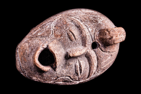 an ancient terracotta vase or jug shaped like a human face isolated over a black backgroundの写真素材