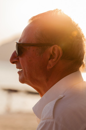 portrait shot of an old man on the beach looking at the sunsetの写真素材