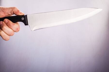 a male hand holding a big kitchen knife over a dark backgroundの写真素材