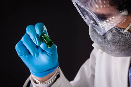 a joung and handsome doctor or researcher with a white lab coat holding a vial with green fluidの写真素材