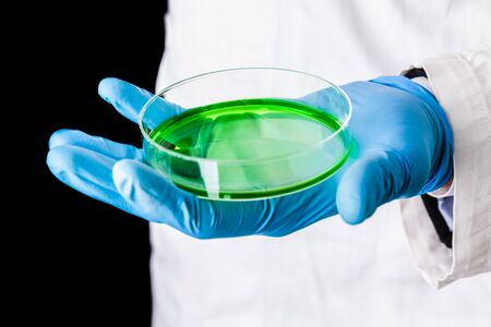 a doctor or researcher with a white lab coat holding a petri dish filled with green liquid