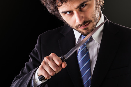an handsome businessman wearing a suit and a tie holding a big kitchen knifeの写真素材