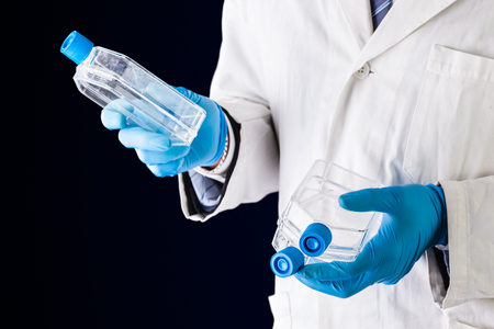 a doctor or researcher with a white lab coat holding a cell culture flaskの写真素材