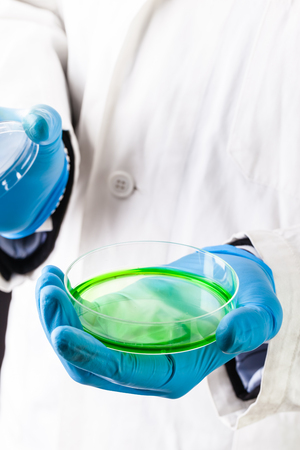 a doctor or researcher with a white lab coat holding a petri dish filled with green gooの写真素材