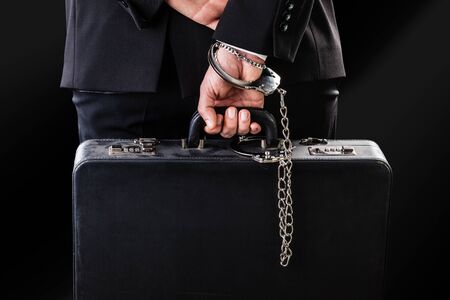 Businessman wearing a suit with a secure suitcase attached with handcuffsの写真素材