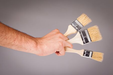 a male hand holding a paintbrush over a light background