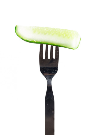 Slice of fresh green cucumber on fork isolated on white background.の写真素材